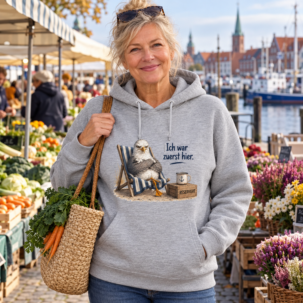 Frau im graumelierten Bio-Hoodie mit Möwe Alpha und Ich war zuerst hier als Frontprint auf einem Hafenmarkt.