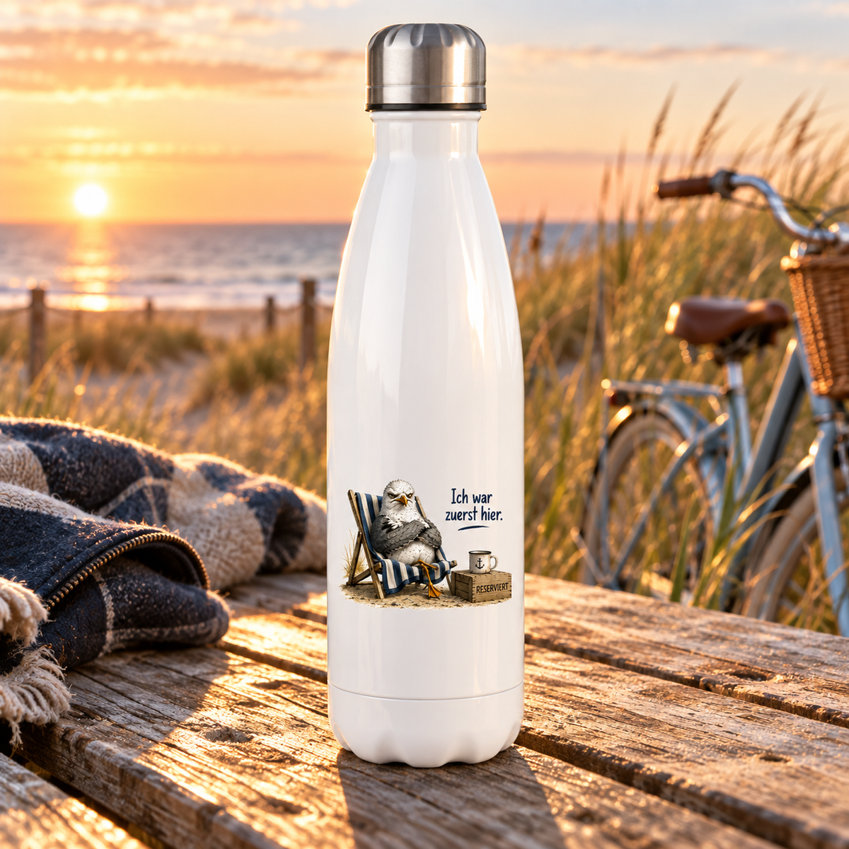 Weiße 500-ml-Thermoflasche mit Möwe im Strandstuhl und Schriftzug Ich war zuerst hier auf einem Tisch an den Dünen.
