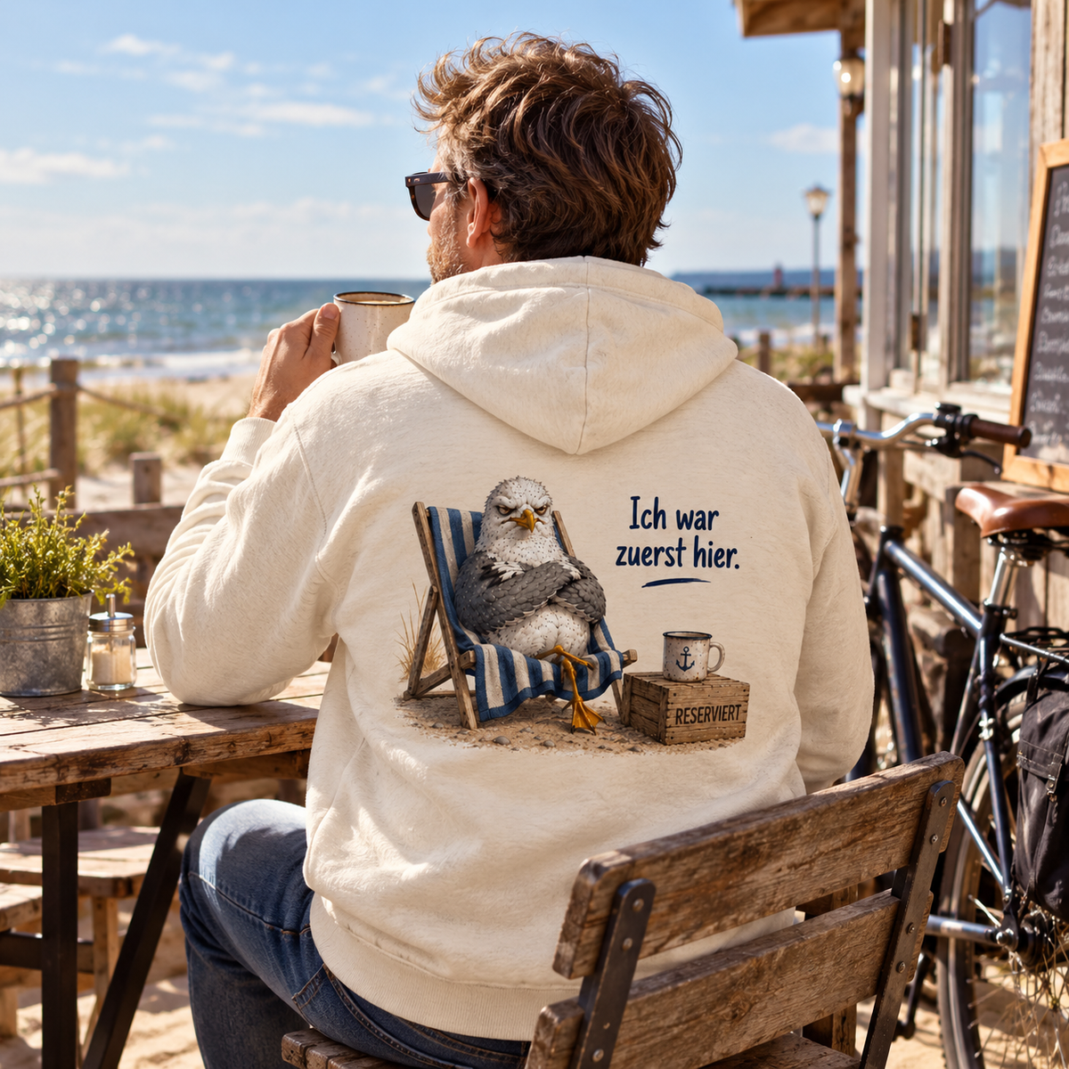 Naturfarbener Bio-Zipper mit Möwe im Strandstuhl als Rückenprint auf einer Terrasse am Meer.