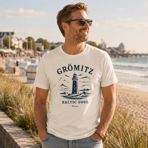 Mann trägt das  Bio-T-Shirt „Baltic Soul“ in der Farbe Natur aus der offiziellen Grömitz-Kollektion von Nomavé an der Grömitzer Strandpromenade – maritimer Küstenlook mit Blick auf die Ostsee.