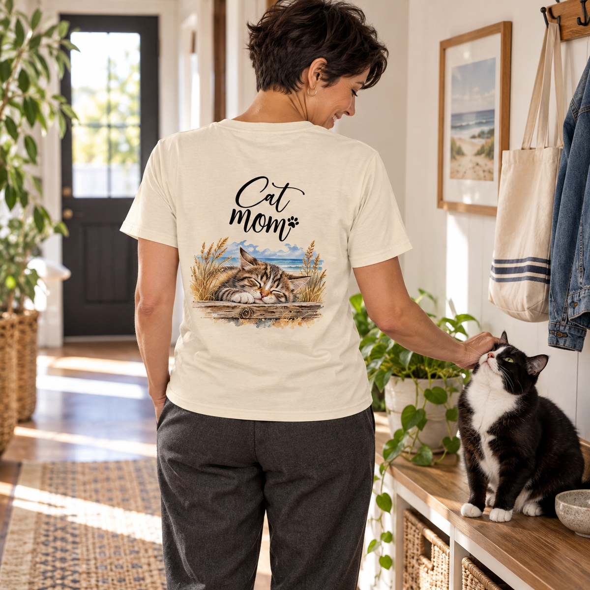 Cat Mom Unisex Bio-T-Shirt in Natural Raw mit Katzenmotiv auf dem Rücken, Frau streichelt eine schwarz-weiße Katze im Flur.
