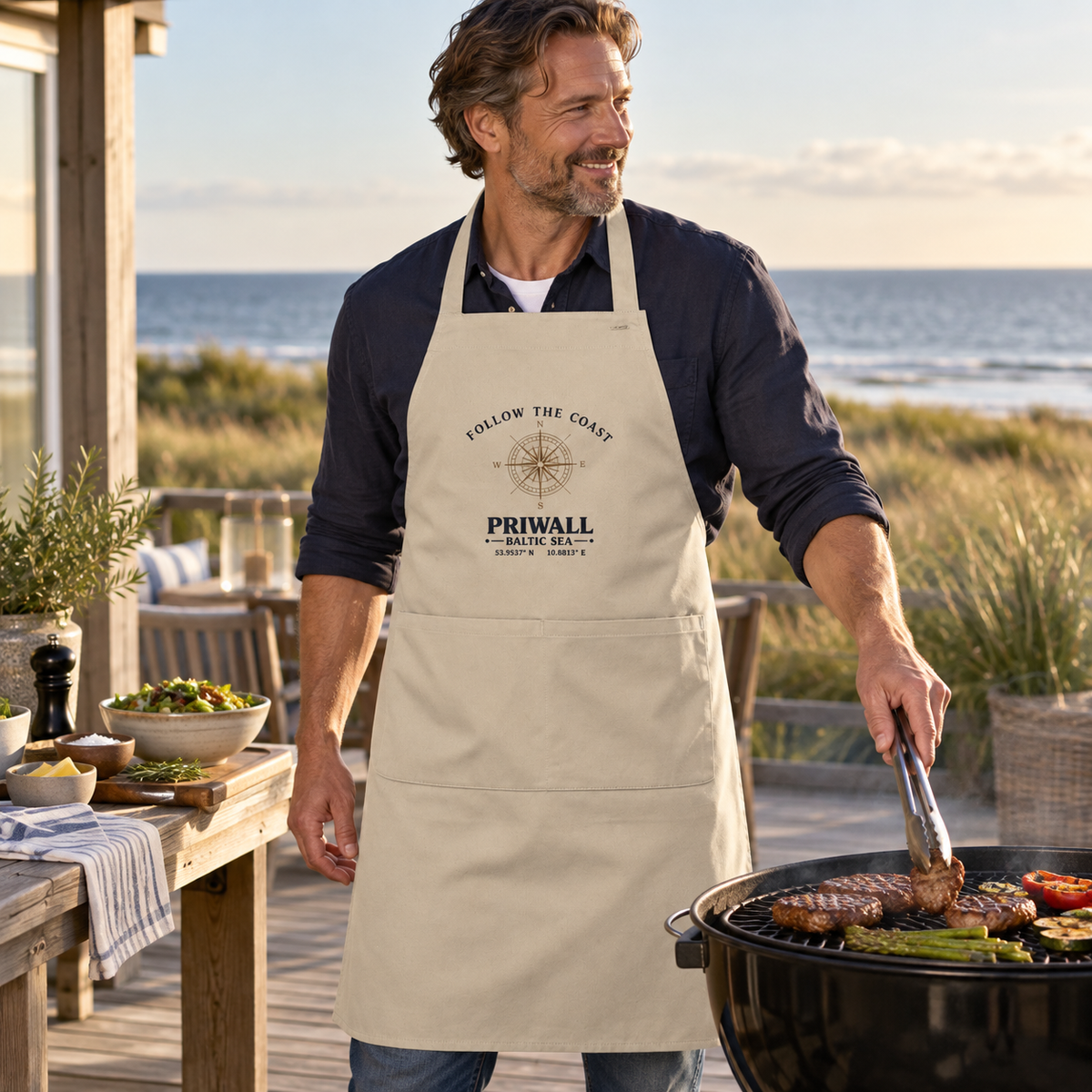 Mann trägt die Follow the Coast Priwall Bio-Grillschürze beim Grillen an der Ostsee