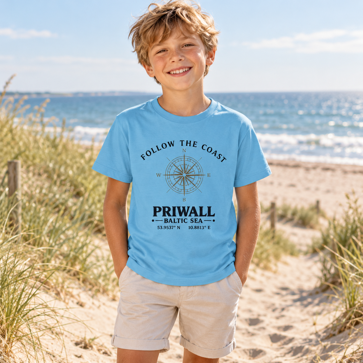 Kind im Aqua Blue Bio-Shirt mit Follow the Coast Priwall Kompass am Ostseestrand