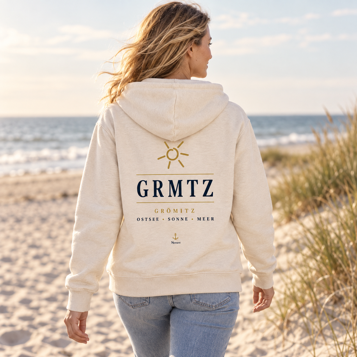 Frau trägt die GRMTZ Grömitz Bio-Zipper-Kapuzenjacke in Natural Raw am Ostseestrand