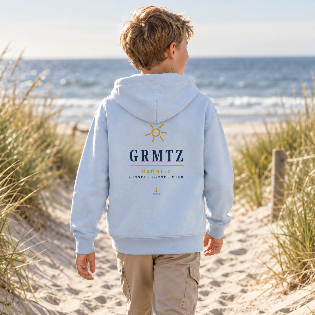 Junge trägt den GRMTZ Grömitz Kinder Bio-Hoodie in Blue Soul am Ostseestrand