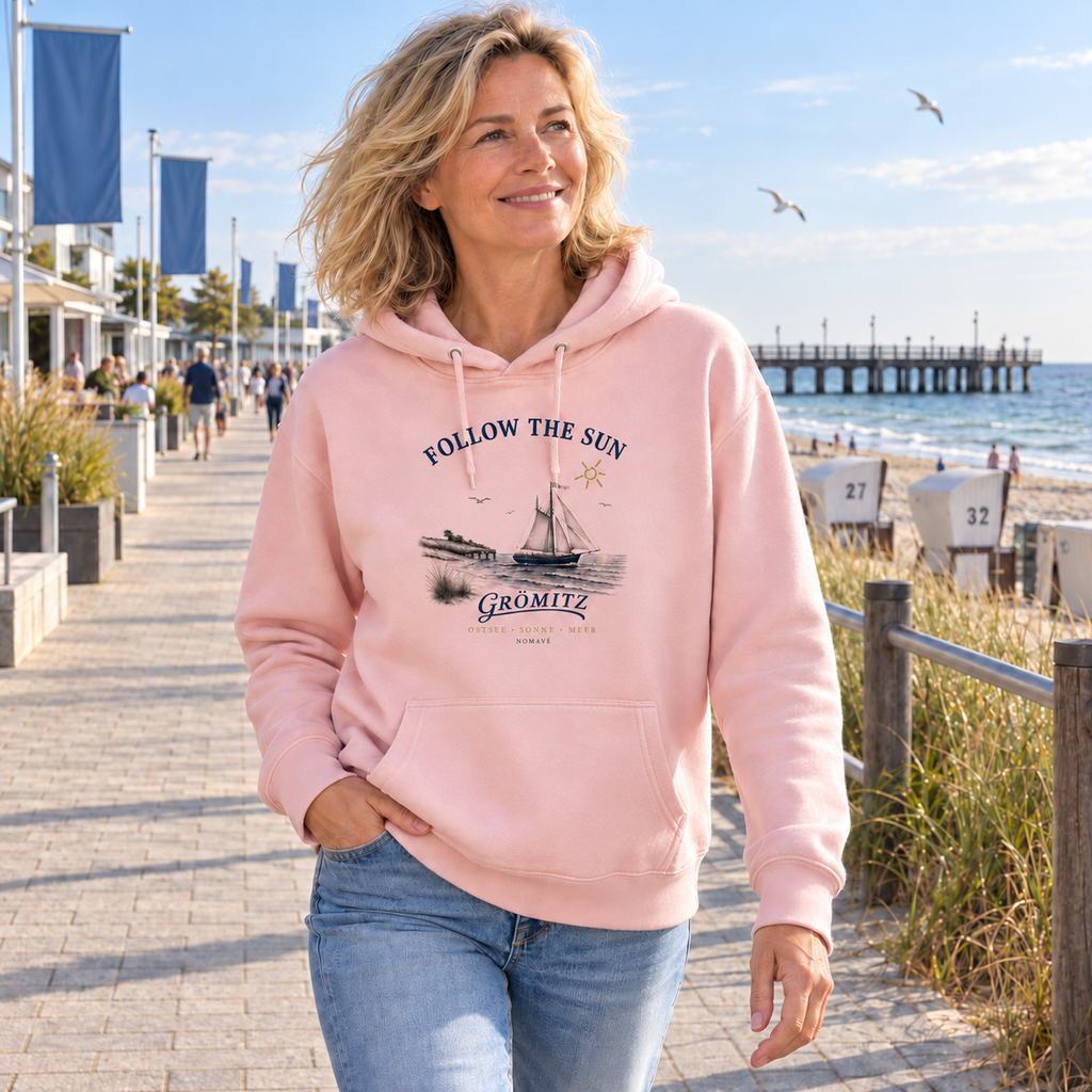 Frau trägt den Cotton-Pink Follow the Sun Grömitz Bio-Hoodie auf einer Ostsee-Promenade