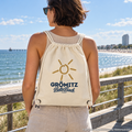 Grömitz Sonne Gym-Bag aus Recycling-Canvas in Natural mit Baltic-Beach-Motivdruck – Frau trägt Beutel als Kordelrucksack an Strandpromenade, KI-Produktvisualisierung
