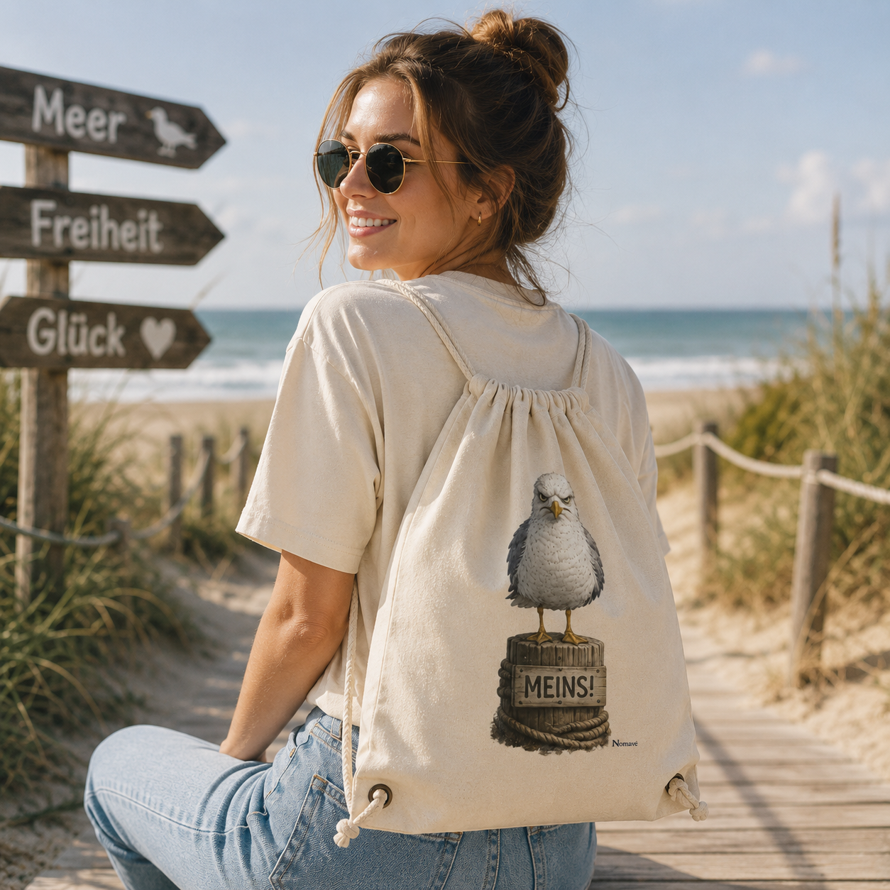 Junge Frau trägt den Nomavé Gymbag „Möwe mit Meinung – MEINS!“ am Strand. Der naturfarbene Turnbeutel mit der frechen Möwe Alpha auf einem Poller eignet sich perfekt für Strand, Urlaub, Freizeit und den Alltag.