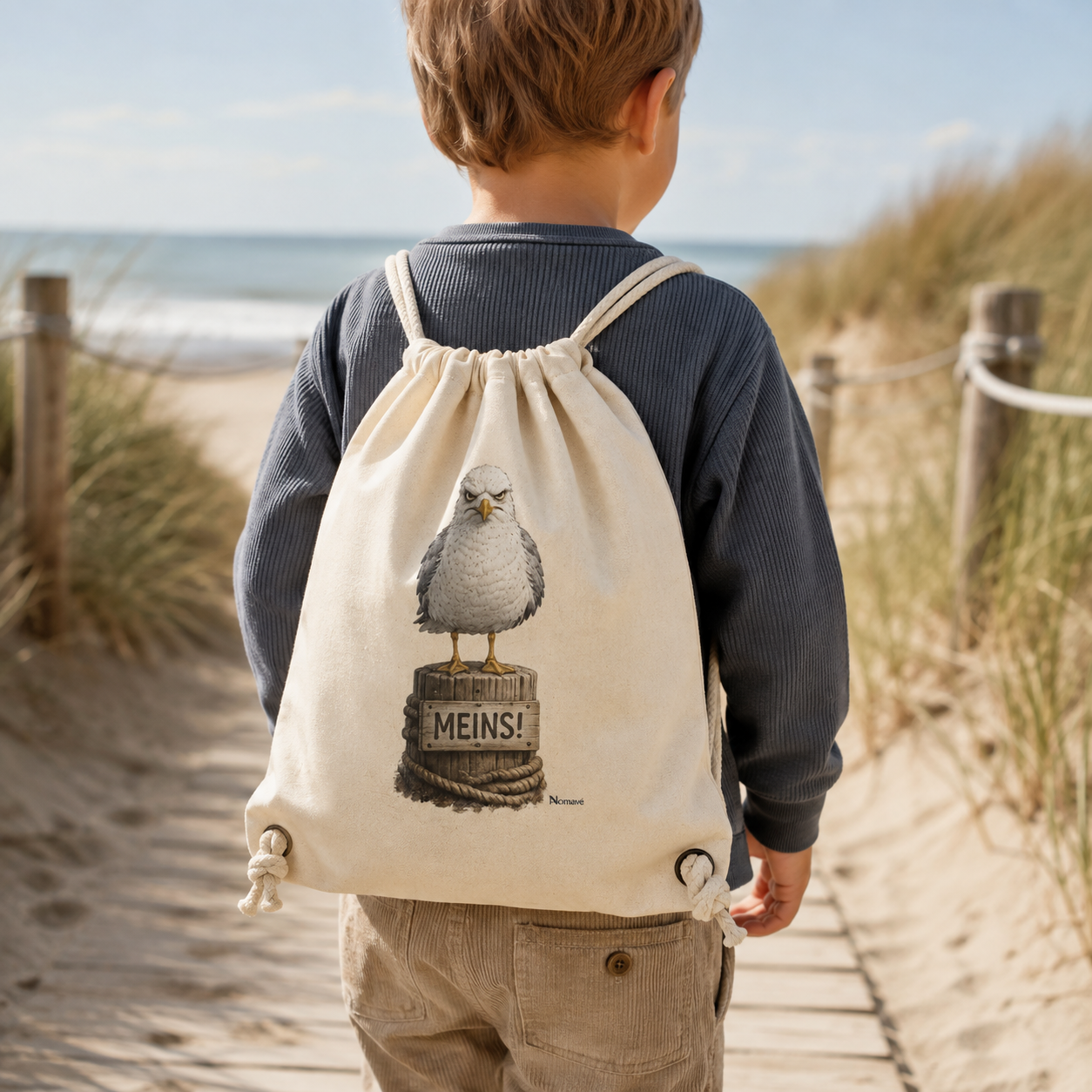 Kind trägt den Gymbag „Möwe mit Meinung – MEINS!“ von Nomavé auf einem Holzsteg durch die Ostseedünen. Der naturfarbene Turnbeutel mit der grimmigen Möwe auf einem Poller verbindet maritimen Küstenstil mit norddeutschem Humor.
