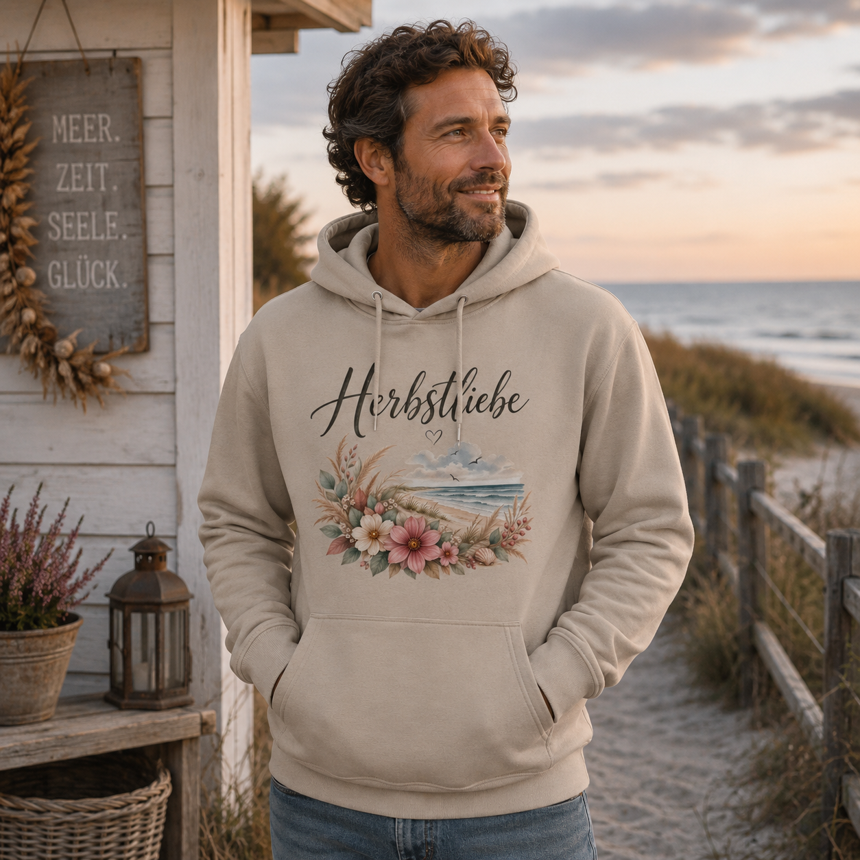 Mann trägt Herbstliebe am Meer Unisex Bio Hoodie in Desert Dust an der Küste