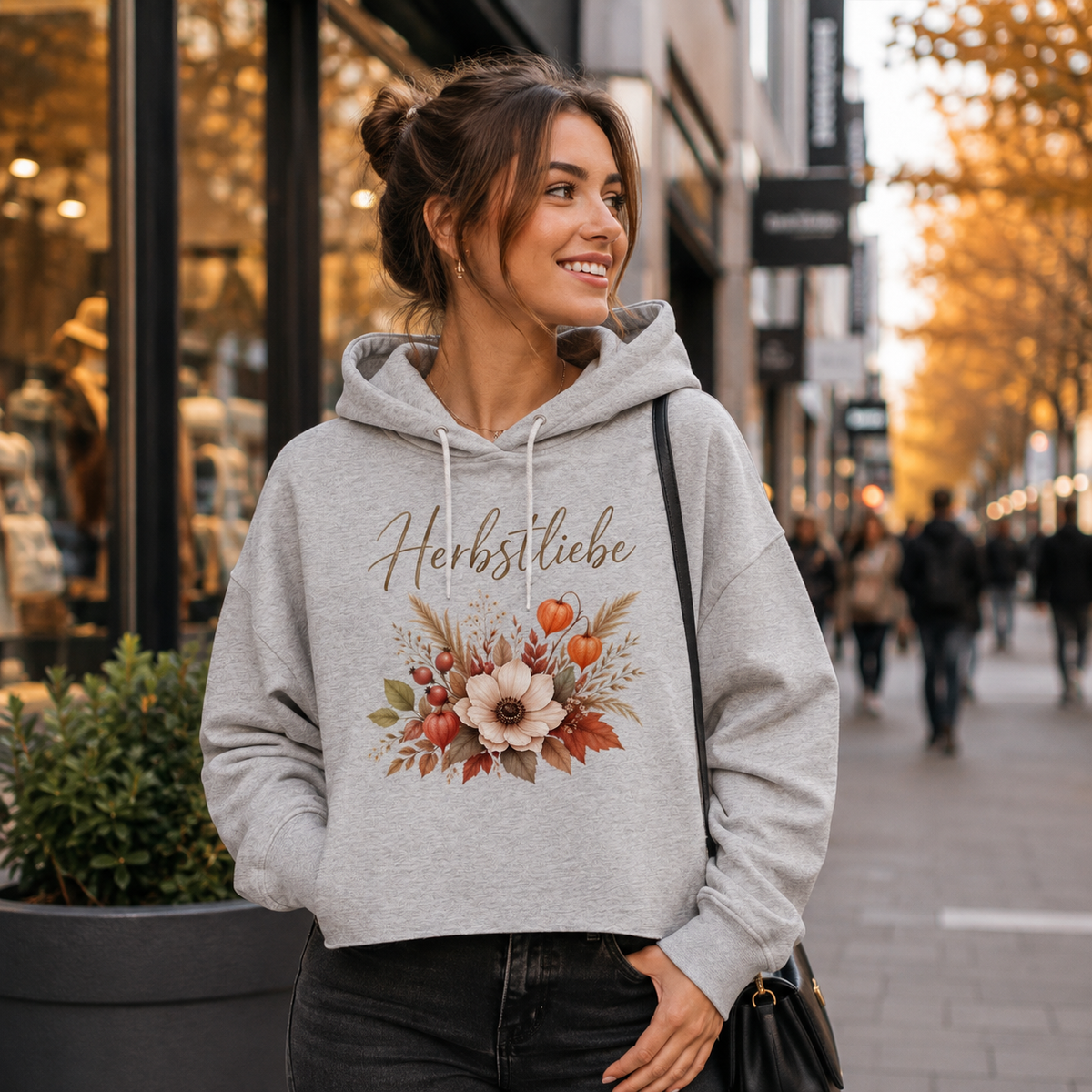 Junge Frau trägt grauen Herbstliebe Golden Harvest Damen Boxcut Hoodie mit floralem Herbstmotiv beim Stadtbummel