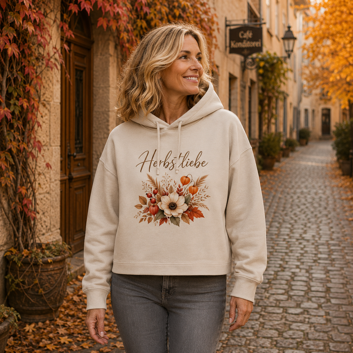 Frau trägt cremefarbenen Herbstliebe Golden Harvest Damen Boxcut Hoodie mit floralem Herbstmotiv in einer herbstlichen Altstadtgasse