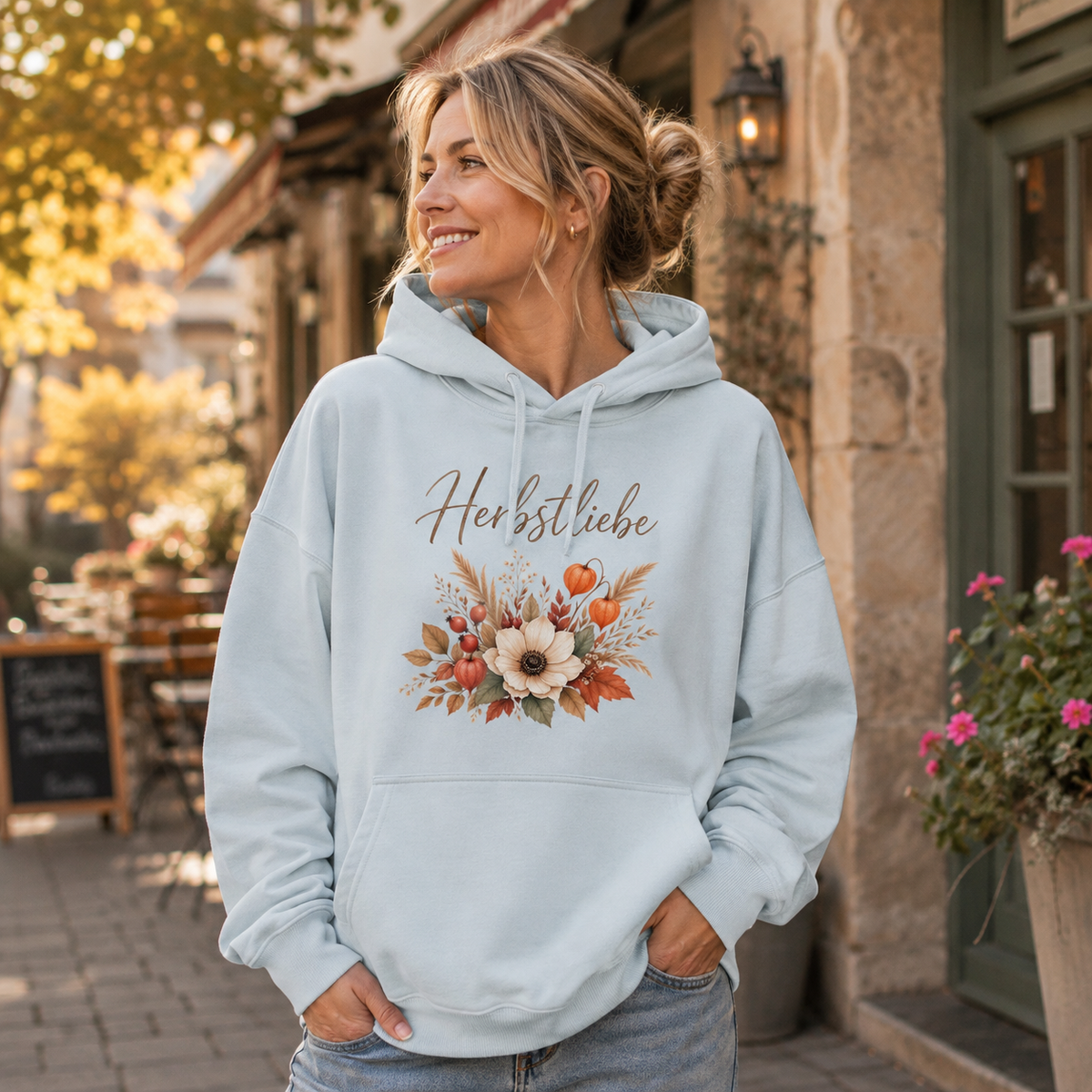 Frau trägt eisblauen Herbstliebe Golden Harvest Oversize Hoodie mit floralem Herbstmotiv in herbstlicher Altstadt