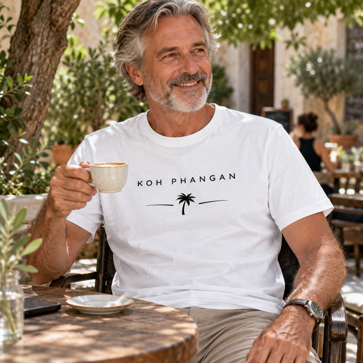 Mann im Bio Heavy T-Shirt mit Koh Phangan Minimal Palm Motiv in einem Restaurantgarten