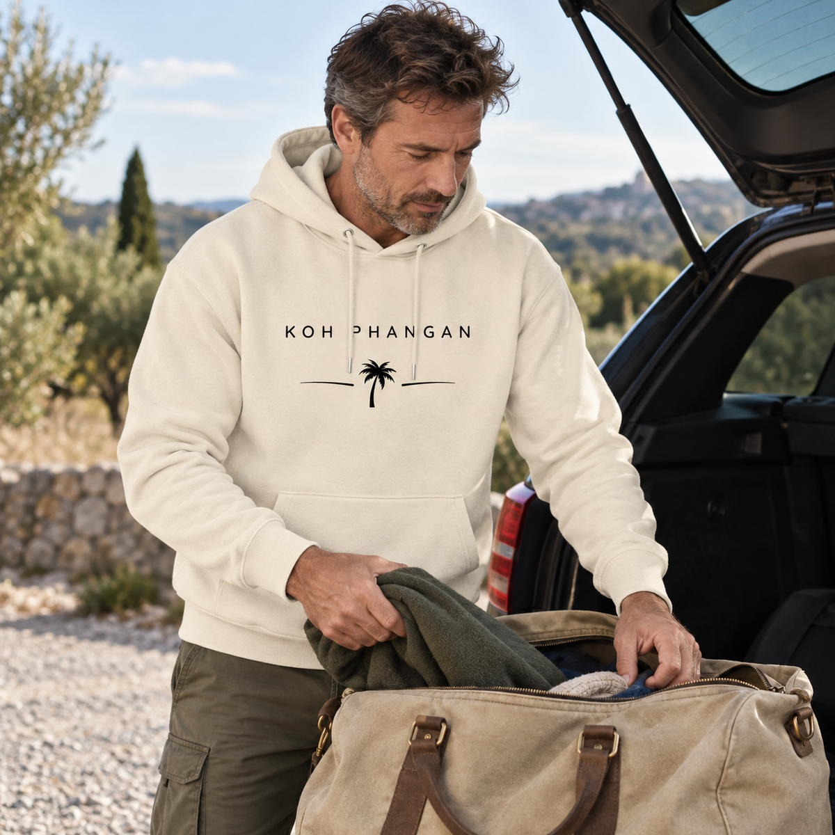 Mann im Bio Hoodie mit Koh Phangan Minimal Palm Frontprint beim Packen für einen Wochenendausflug