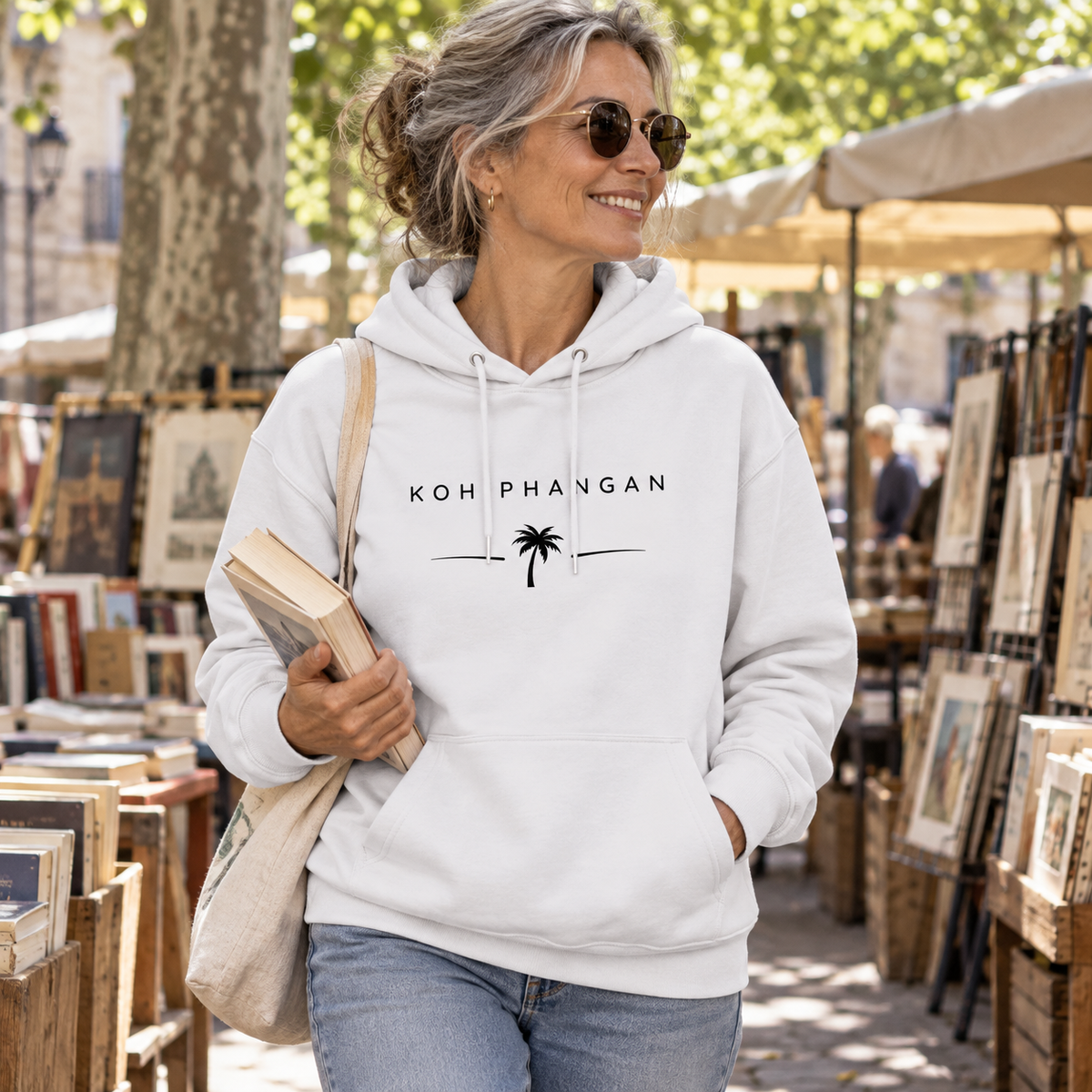 Frau im Bio Hoodie mit Koh Phangan Minimal Palm Motiv auf einem Büchermarkt