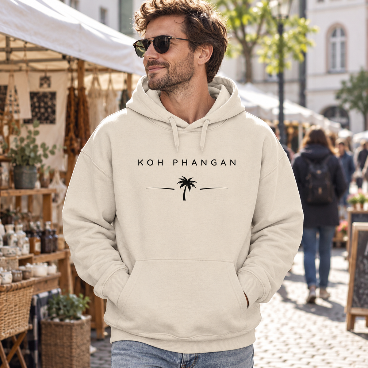 Mann im Bio Oversize Hoodie mit Koh Phangan Minimal Palm Motiv auf einem Stadtmarkt