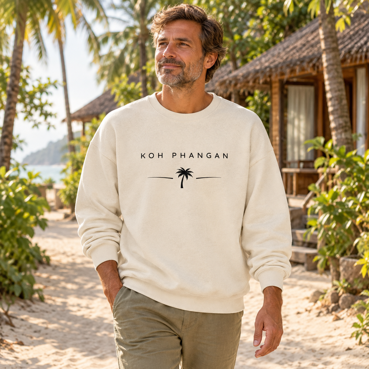 Mann im Bio Oversize Sweatshirt mit Koh Phangan Minimal Palm Frontprint auf einer Inselpromenade