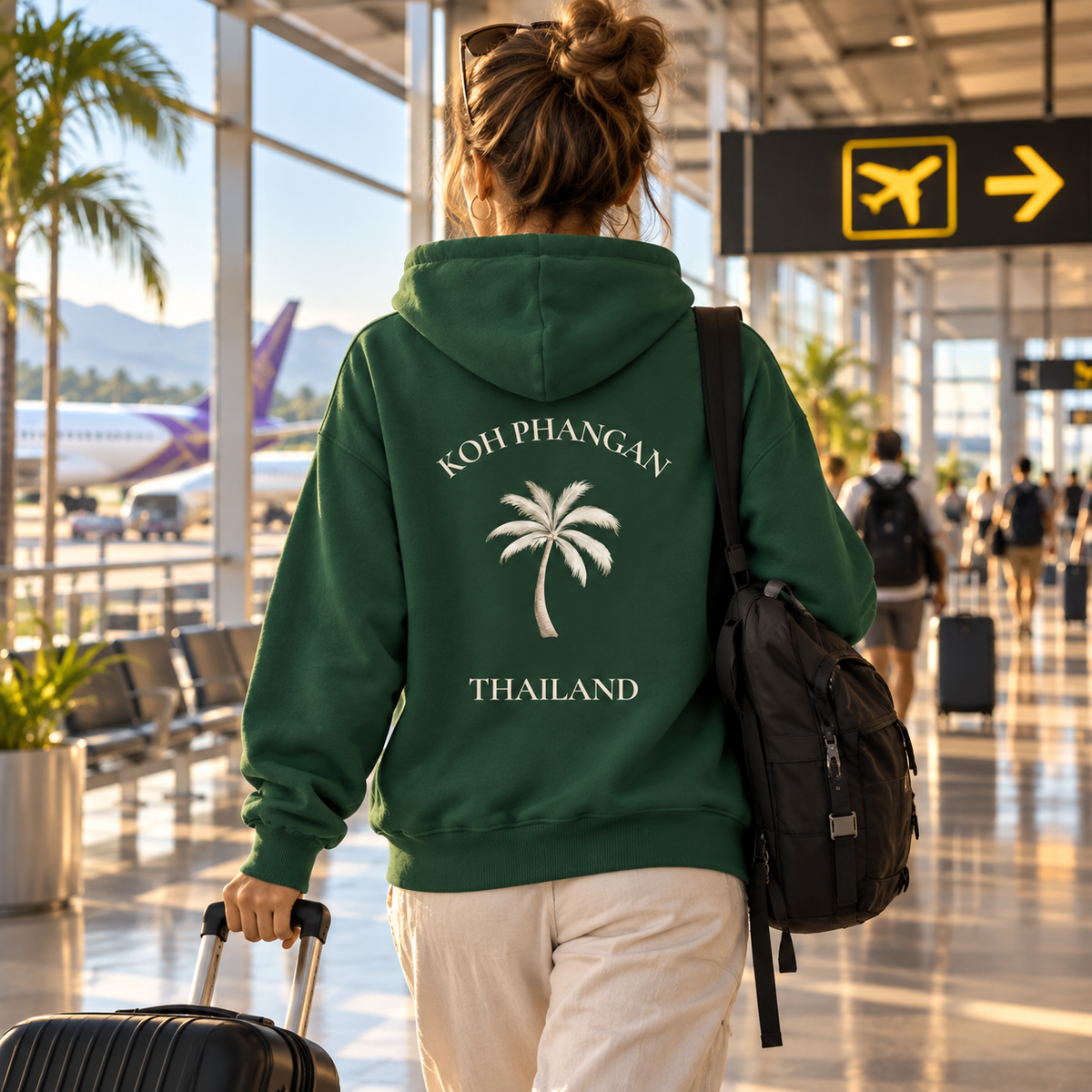 Bio Side Pocket Hoodie mit Koh Phangan Mini Palm Backprint in einer Abflughalle mit Reisegepäck