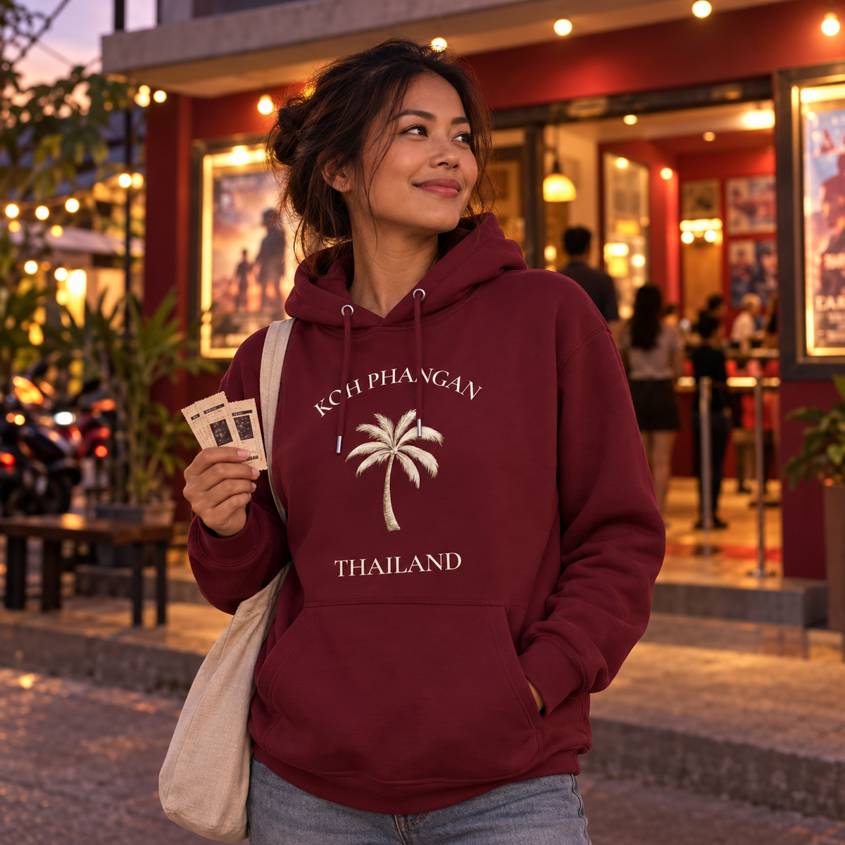 Frau im Burgundy Bio Hoodie mit Koh Phangan Mini Palm Frontprint vor einem Kino in Thailand