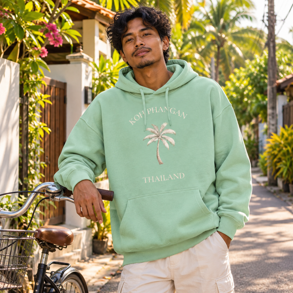 Mann im Misty Jade Bio Oversize Hoodie mit Koh Phangan Mini Palm Frontprint an einer thailändischen Wohnstraße