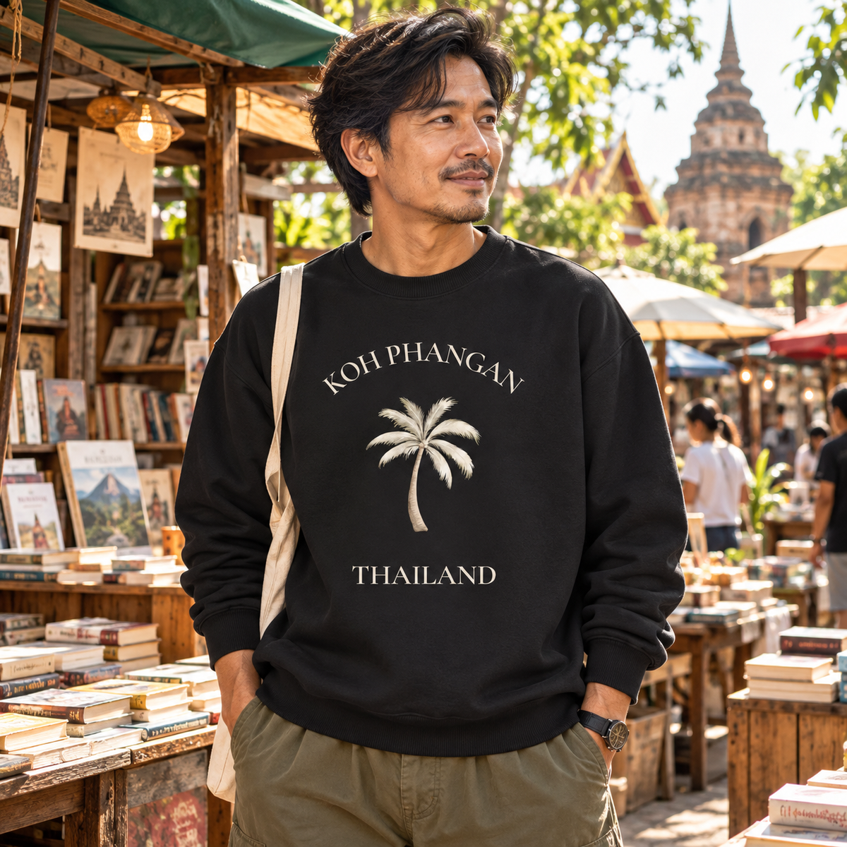 Mann in schwarzem Bio Oversize Sweatshirt mit Koh Phangan Mini Palm Frontprint auf einem thailändischen Büchermarkt