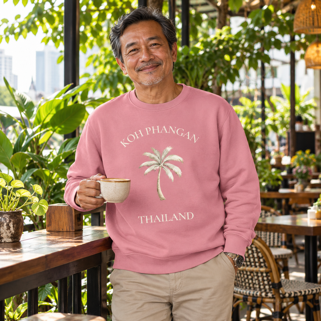 Mann im Canyon Pink Bio Unisex Sweatshirt mit Koh Phangan Mini Palm Frontprint in einem thailändischen Gartencafé