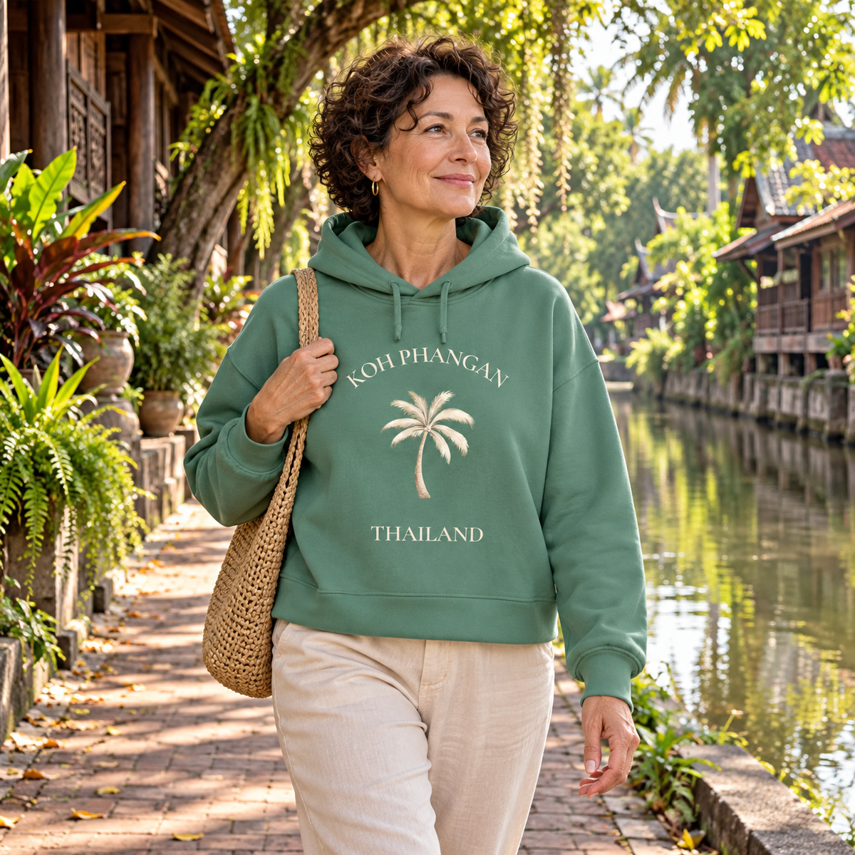 Frau im Green Bay Damen Bio Boxcut Hoodie mit Koh Phangan Mini Palm Frontprint an einer thailändischen Kanalstraße