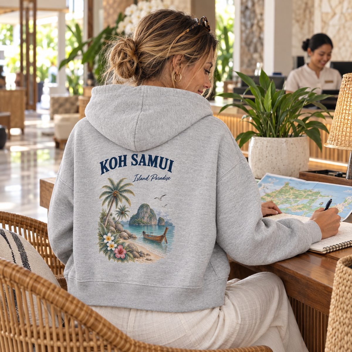 Frau im grauen Damen Bio Boxcut Hoodie mit Koh Samui Island Paradise Rückenprint bei der Reiseplanung