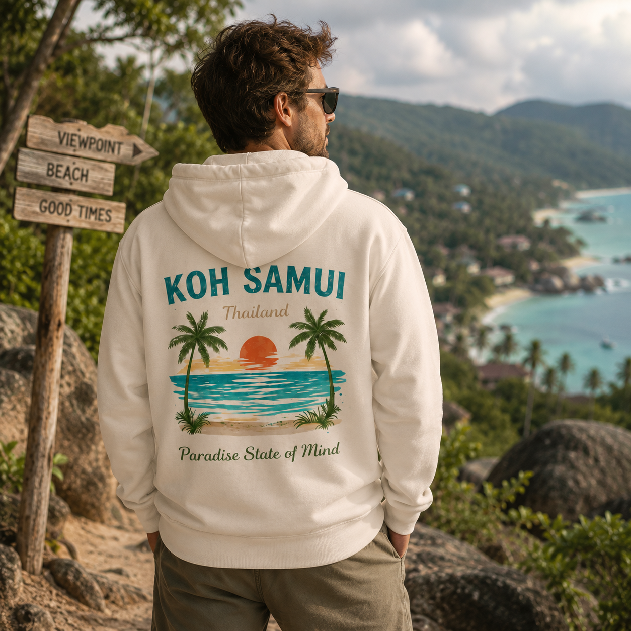 Junger Mann trägt weißen Bio Hoodie mit Koh Samui Thailand Rückenprint an einem Aussichtspunkt über einer tropischen Bucht mit türkisblauem Meer und Palmen – Lifestylebild Paradise State of Mind.