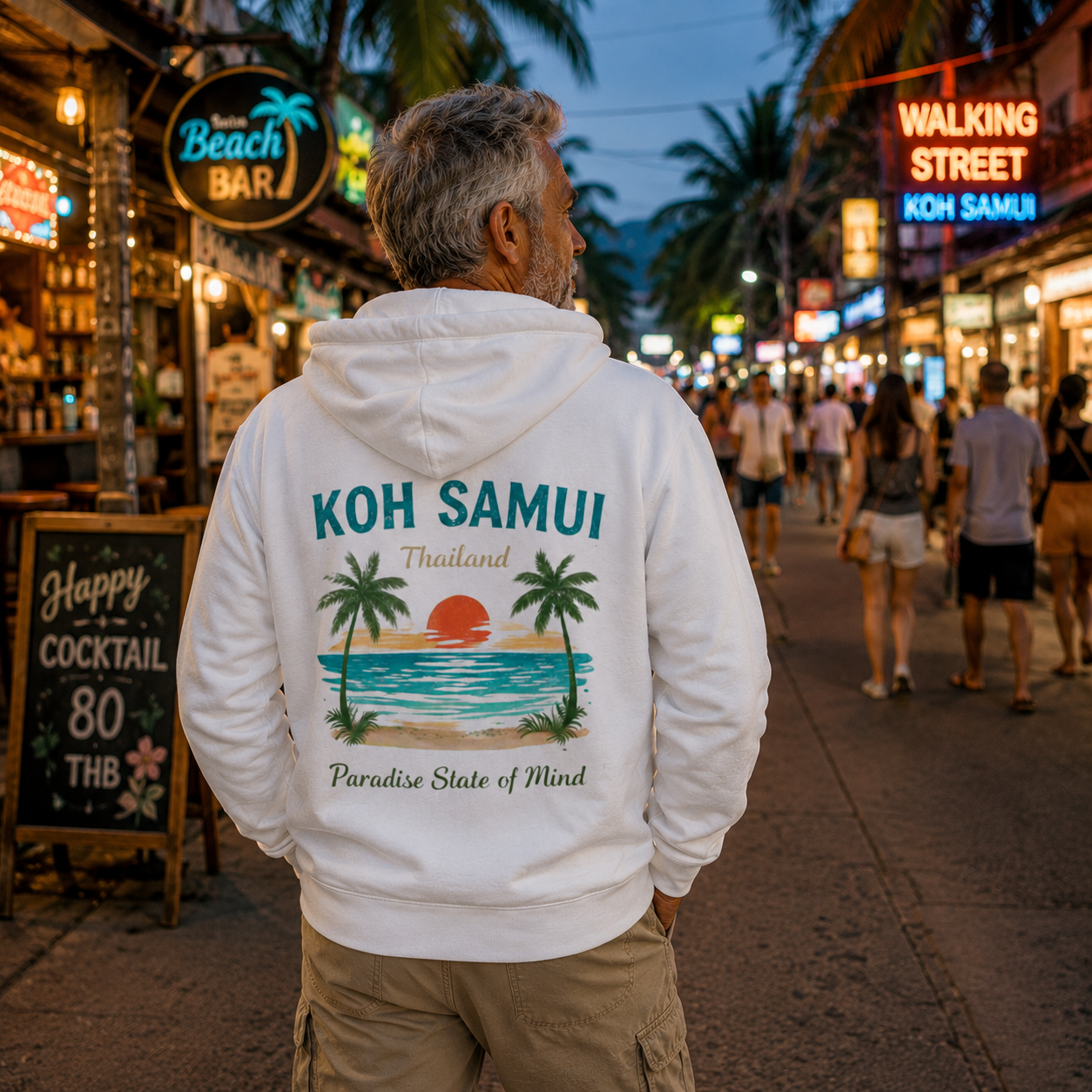 Älterer Mann trägt weißen Bio Hoodie mit Koh Samui Thailand Rückenprint auf einer lebhaften Walking Street in Thailand mit tropischen Lichtern, Palmen und Abendstimmung – Lifestylebild Paradise State of Mind.