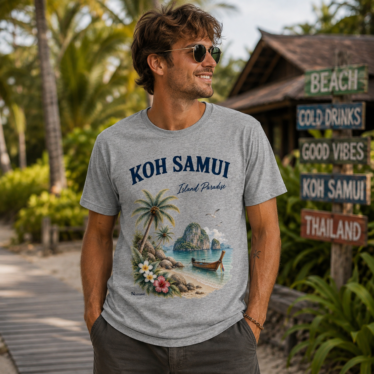 Junger Mann trägt graues Nomavé Koh Samui Island Paradise T-Shirt mit tropischem Thailand-Motiv aus Palmen, Longtailboot und Meer.