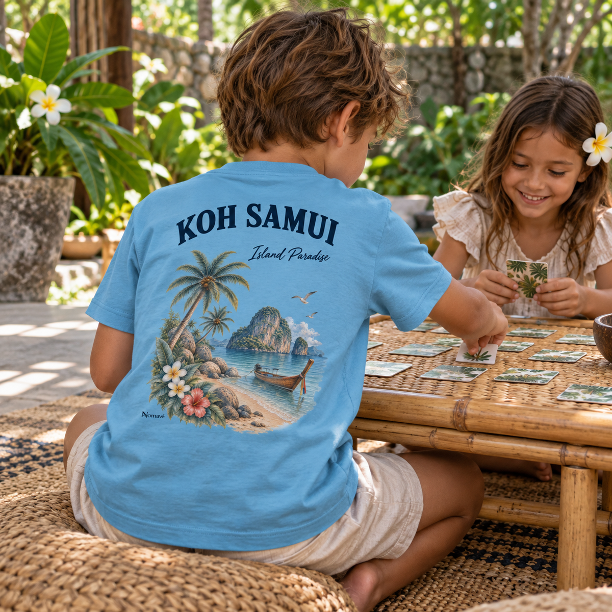 Kind im Caribbean-Blue Kinder Bio T-Shirt mit Koh Samui Island Paradise Rückenprint beim Gartenspiel