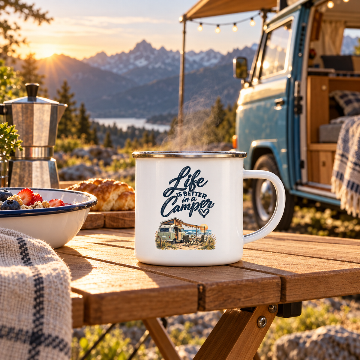 Emaille-Camperbecher mit Life-is-better-in-a-Camper-Motiv beim Frühstück vor blauem Vintage-Camper in den Bergen