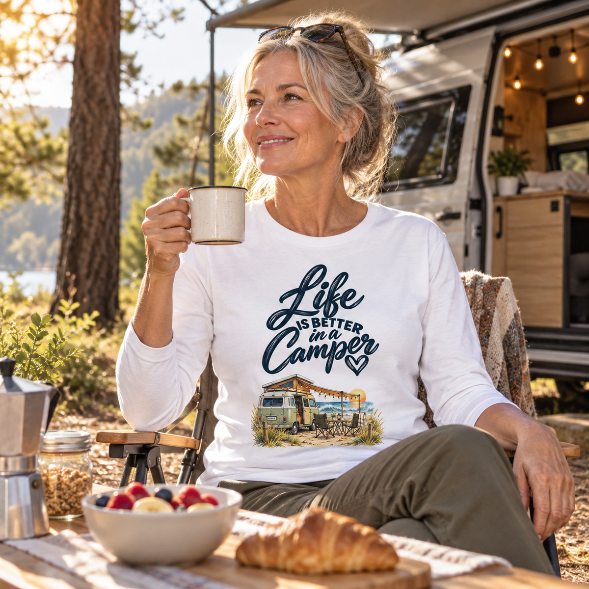 Frau im weißen Bio-Longsleeve mit Camper-Motiv beim Frühstück auf einer Waldlichtung