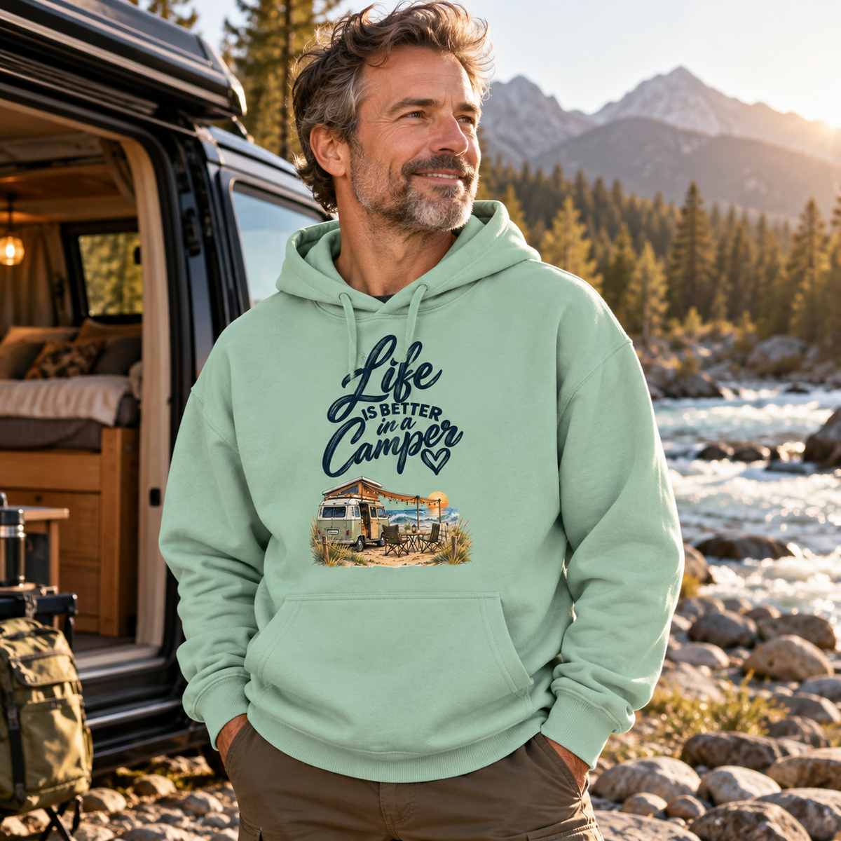 Mann im Misty-Jade Bio-Oversize-Hoodie mit Camper-Motiv am felsigen Flussufer