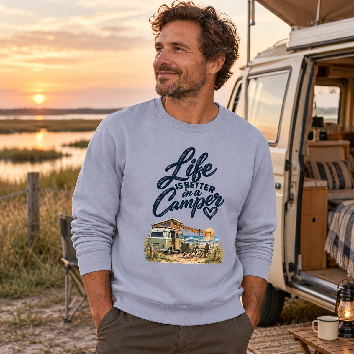 Mann im Serene-Blue Bio-Unisex-Sweatshirt mit Camper-Motiv auf einem Stellplatz im Marschland