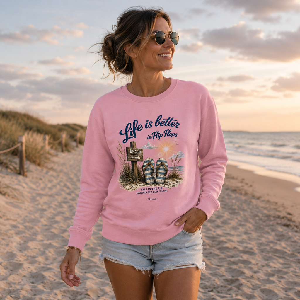 Frau trägt rosa Sweatshirt „Life is Better in Flip Flops“ und spaziert am Ostseestrand entlang der Dünen bei Sonnenuntergang.