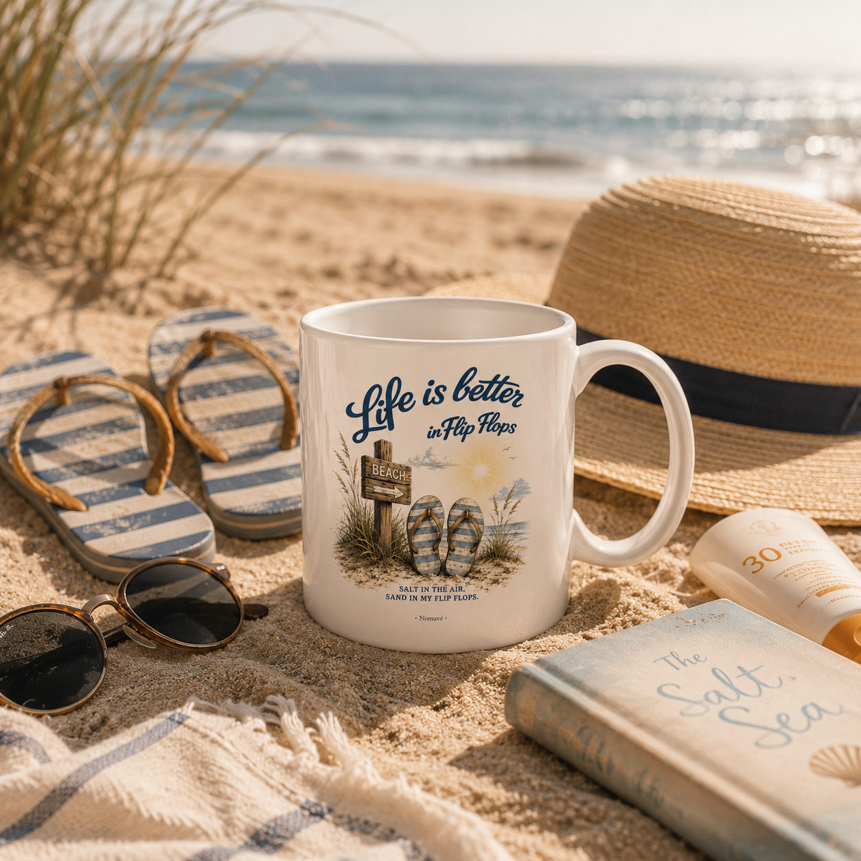 Nomavé Keramiktasse „Life is Better in Flip Flops“ am Ostseestrand zwischen Flip-Flops, Sonnenhut und Strandaccessoires im warmen Morgenlicht – maritimer Küsten-Lifestyle.