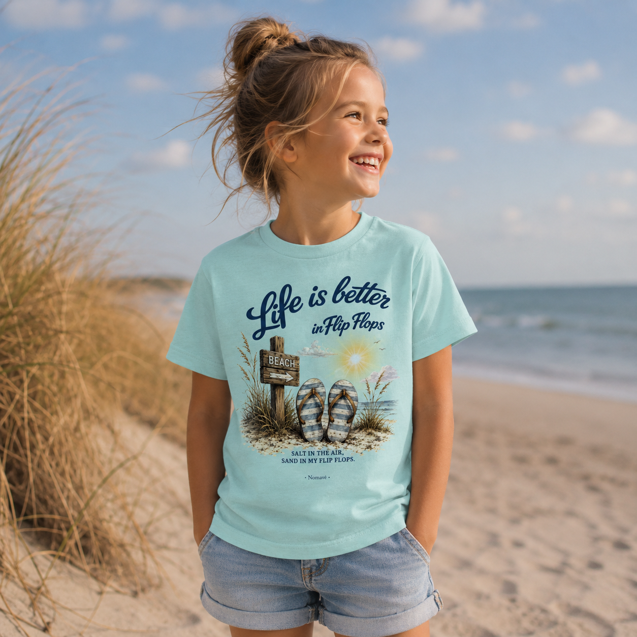 Kind trägt das Nomavé Kinder-T-Shirt „Life is Better in Flip Flops“ am Ostseestrand mit Dünen und Meer im Hintergrund.