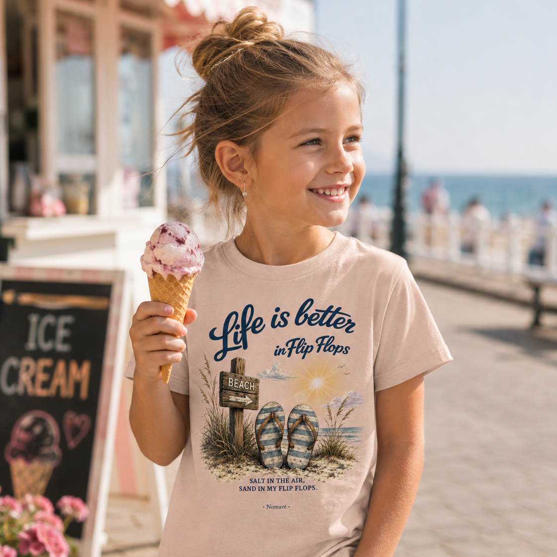 Mädchen trägt das Nomavé Kinder-T-Shirt „Life is Better in Flip Flops“ und genießt ein Eis auf der Ostsee-Promenade an einem sonnigen Tag.
