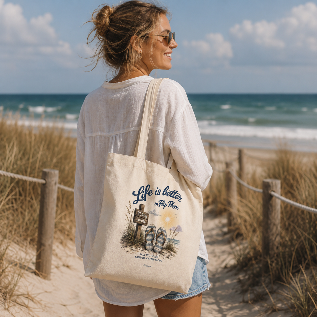 Frau trägt die Nomavé Stofftasche „Life is Better in Flip Flops“ auf einem Strandweg an der Ostseeküste mit Blick auf das Meer.
