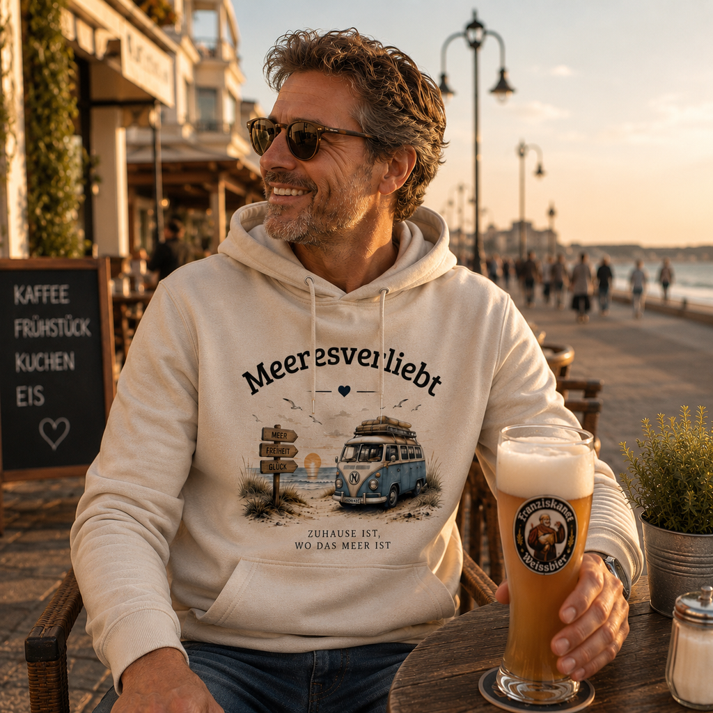Mann im cremefarbenen Meeresverliebt Hoodie sitzt mit einem Getränk in einem Straßencafé an der Ostsee und genießt den Sonnenuntergang