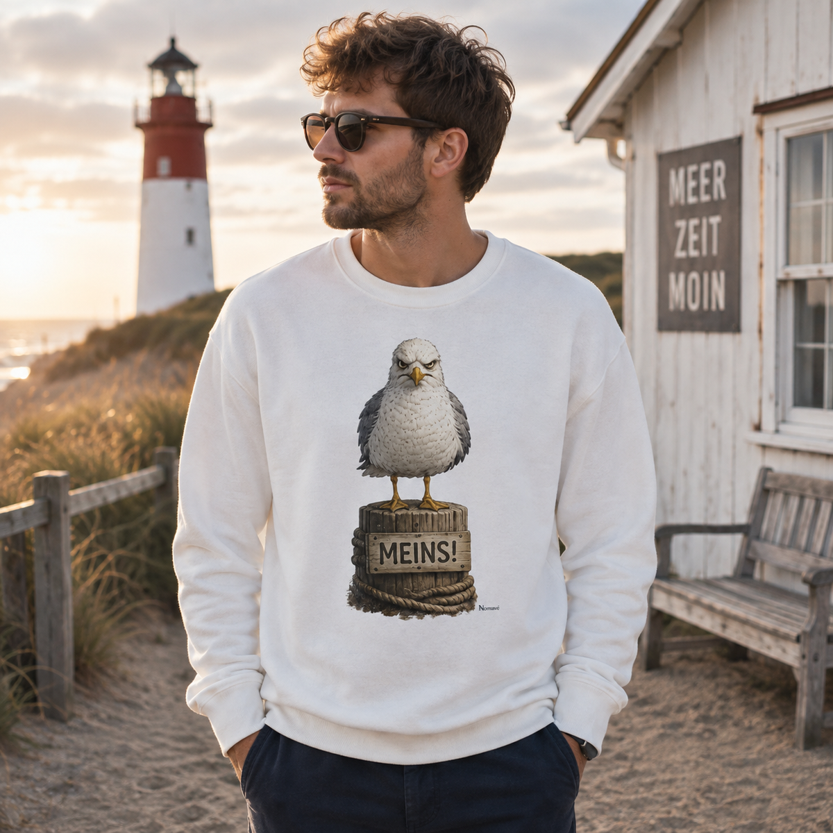 Mann trägt weißes Nomavé Möwen Sweatshirt mit MEINS Motiv an der Küste – maritimer Küstenhumor für Ostsee- und Nordseefans