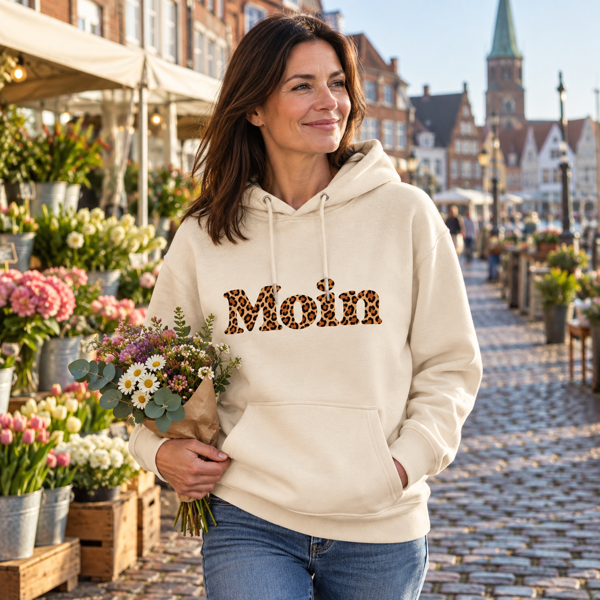Frau im naturfarbenen Bio Hoodie mit lesbarem Moin-Leoprint auf einem Blumenmarkt