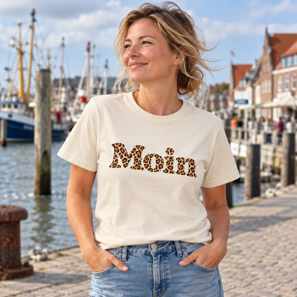 Frau im naturfarbenen Bio Unisex T-Shirt mit lesbarem Moin-Schriftzug im Karamell-Leoprint am Hafen