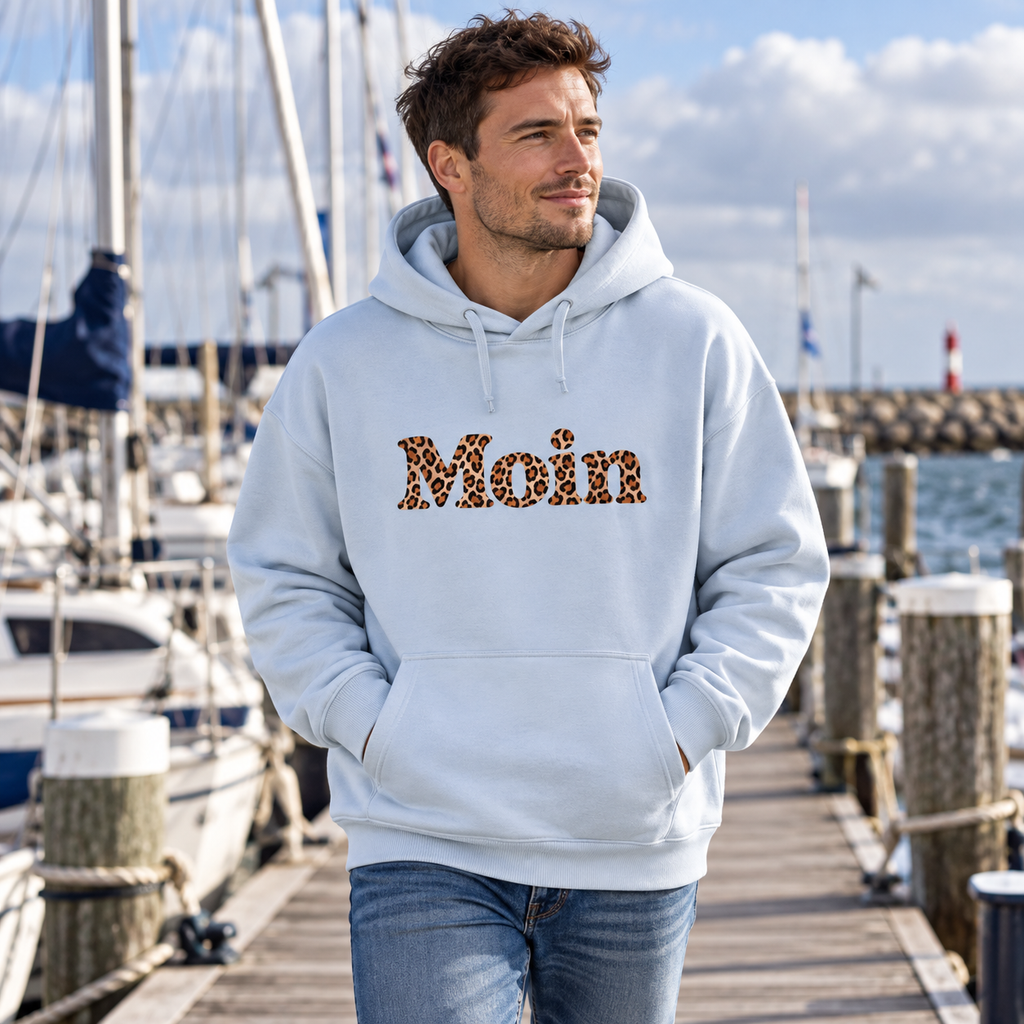 Mann im hellblauen Bio Oversize Hoodie mit Moin-Leoprint auf einem Marinasteg