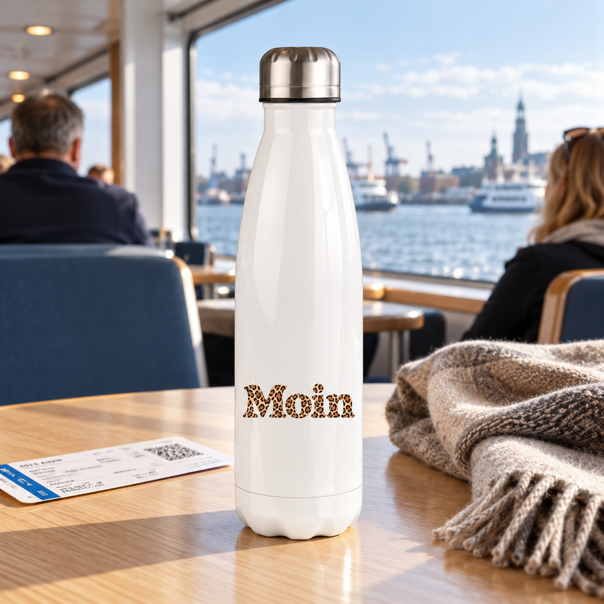 Weiße Moin-Leo-Thermoflasche mit Karamell-Leoprint auf einem Tisch in einer Fährlounge