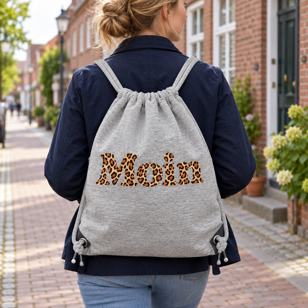Frau trägt die Gym-Bag in Heather Grey mit Moin-Karamell-Leoprint und Kordeln auf dem Rücken in einer Backsteinstraße