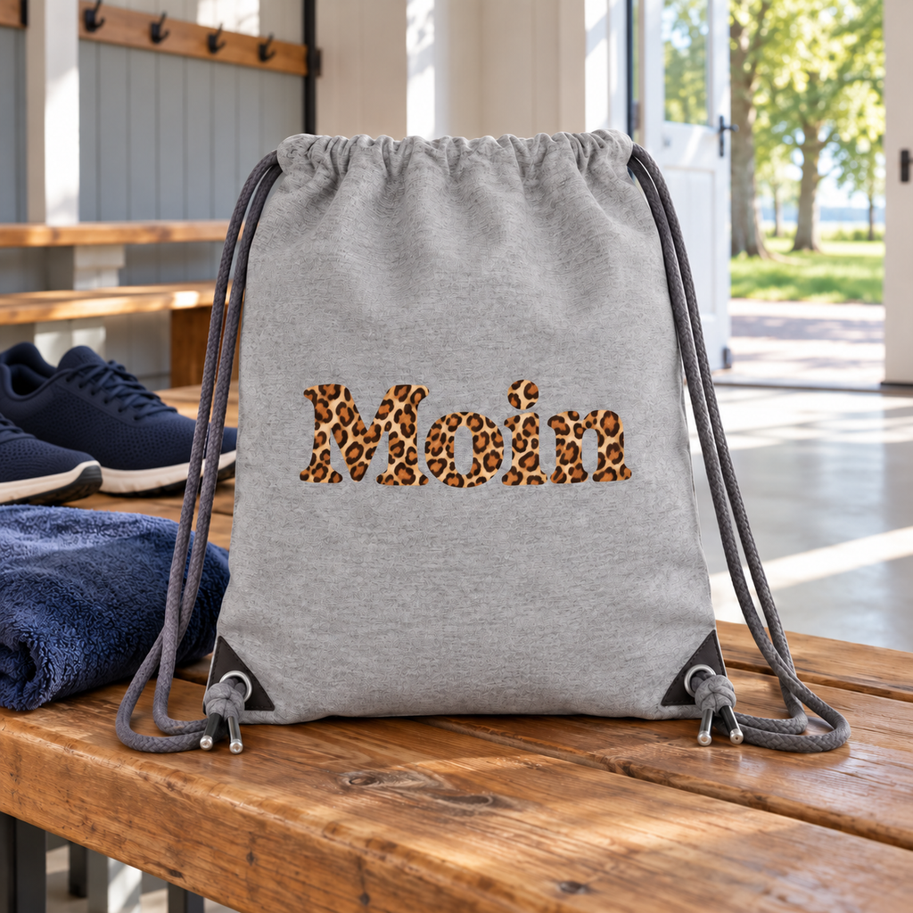 Gym-Bag in Heather Grey mit Moin-Karamell-Leoprint, Zugkordeln und verstärkten Ecken auf einer Holzbank